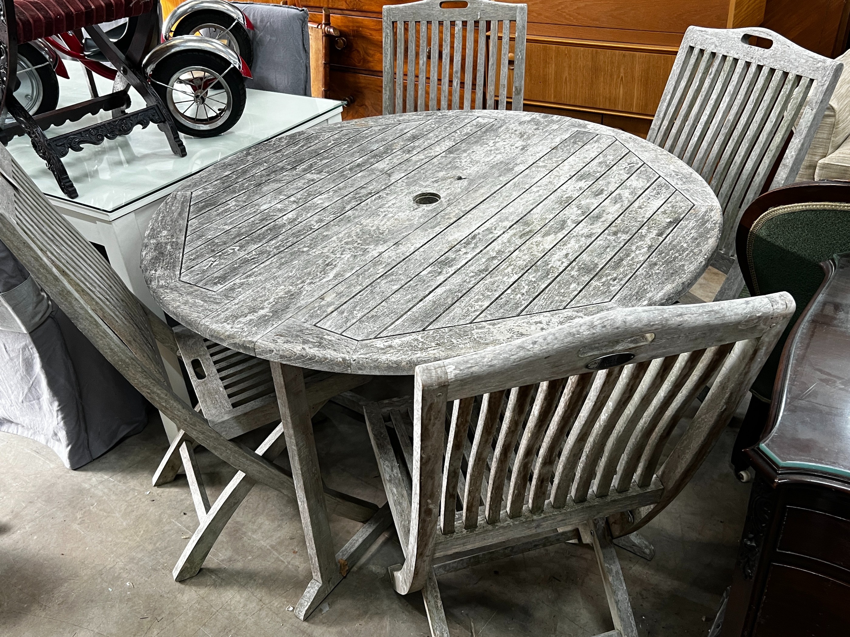 A Jo Alexander circular weathered teak folding garden table, diameter 120cm, height 75cm and four chairs *Please note the sale commences at 9am.